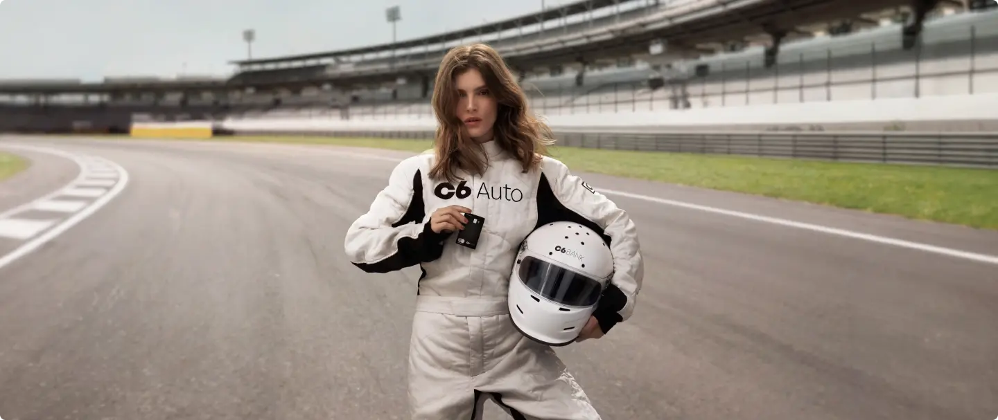 Mulher em autódromo com cartão S 26-27 Mulher em pista de corrida com arquibancada ao fundo, usando macacão de automobilismo com o logo C6 Auto, segurando capacete e cartão C6 Carbon na cor preta.