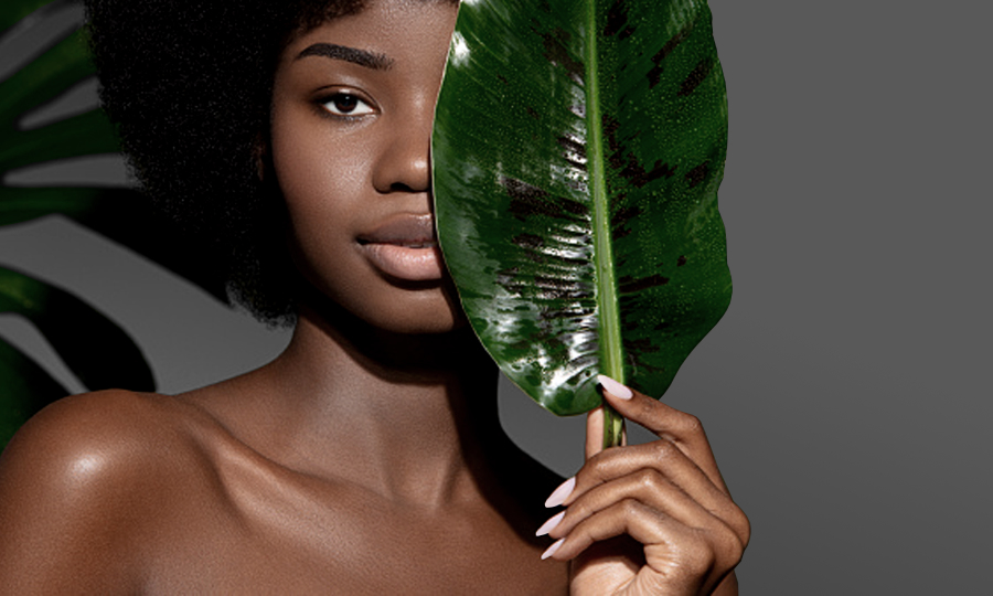 Mulher negra de frente segurando folha de bananeira em frente ao rosto