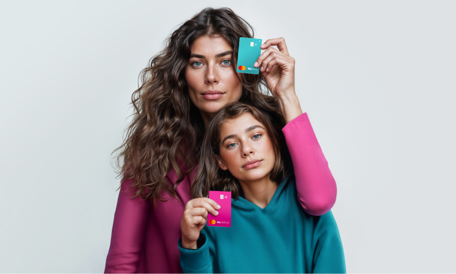 Fotografia de mãe e filha, com fundo branco, cada uma segurando um cartão, sendo a mãe um azul e a filha um rosa. A cor das suas blusas são rosa e azul respectivamente.