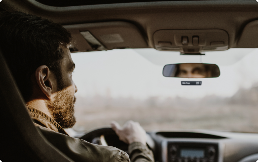 Fotografia tirada dentro de um carro, onde aparece o motorista olhando para o retrovisor.