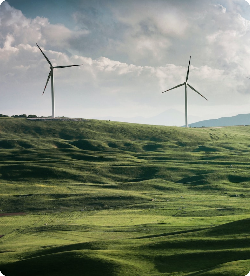 Colinas verdes com duas turbinas eólicas sob céu nublado, representando energia sustentável.