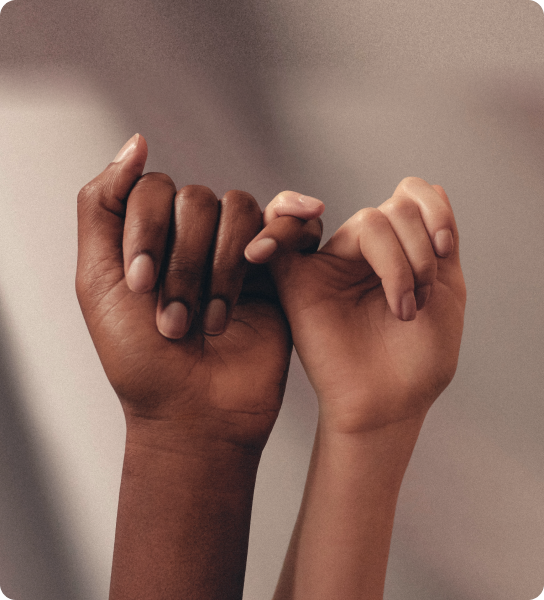 Duas mãos de tons de pele diferentes com dedos mínimos entrelaçados, representando união e diversidade.