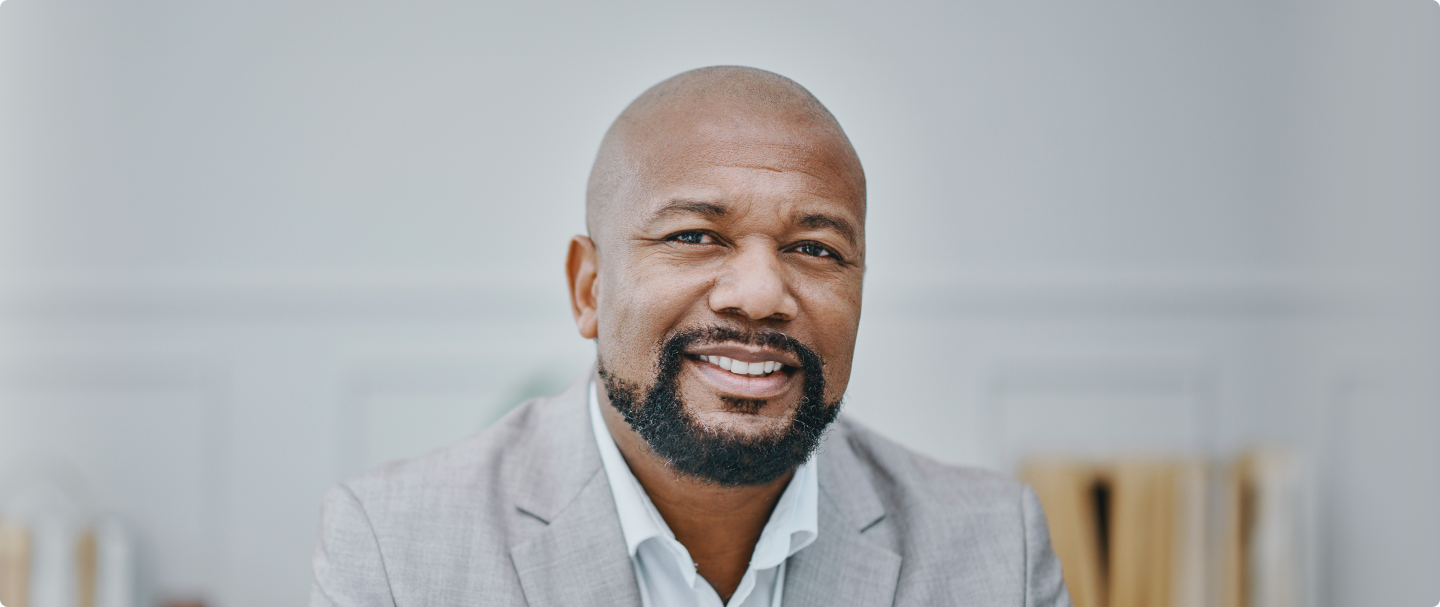 Fotografia de homem negro com bigode e careca usando um blazer e blusa social