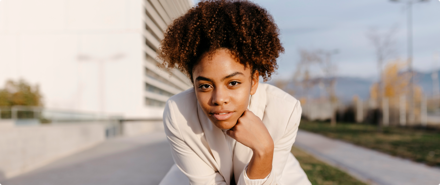 Fotografia de mulher negra com terno branco e cabelo preso olhando para a câmera