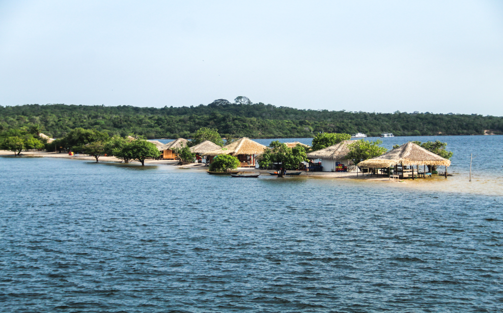 Vista de uma bela ilha com cabanas de palha ao redor de água clara, cercada por vegetação tropical, criando um ambiente sereno e tranquilo.