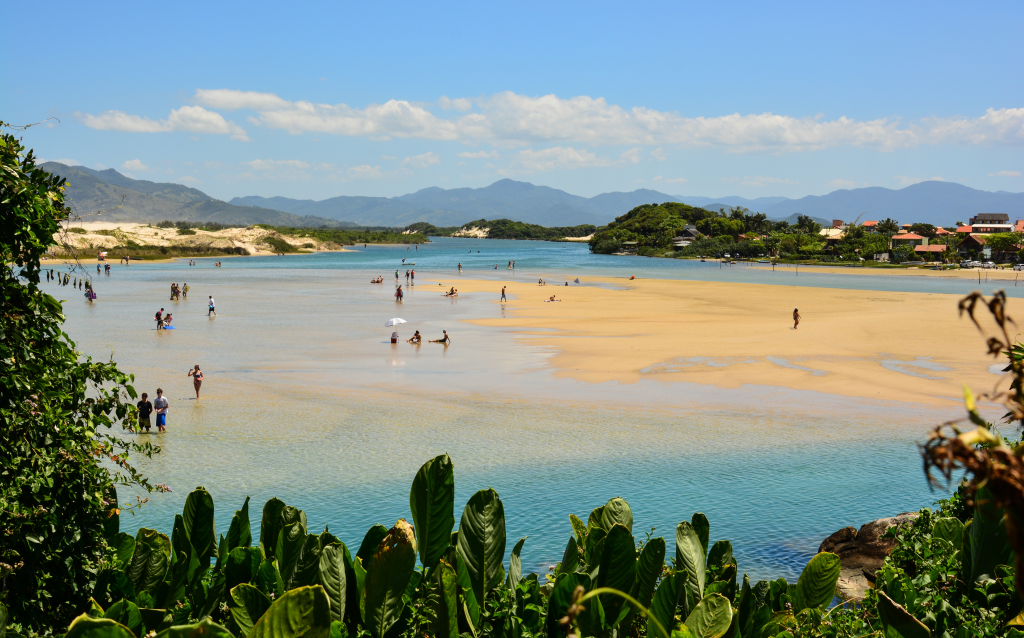 Vista deslumbrante de uma praia com água cristalina, areia clara e pessoas se divertindo, ideal para um dia de lazer ao ar livre em contato com a natureza.