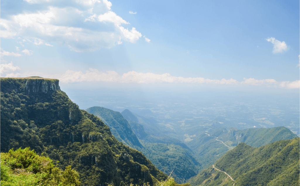 Vista das montanhas e cânions no Parque Nacional da Serra Geral, Rio Grande do Sul, com vegetação densa e estrada ao fundo.