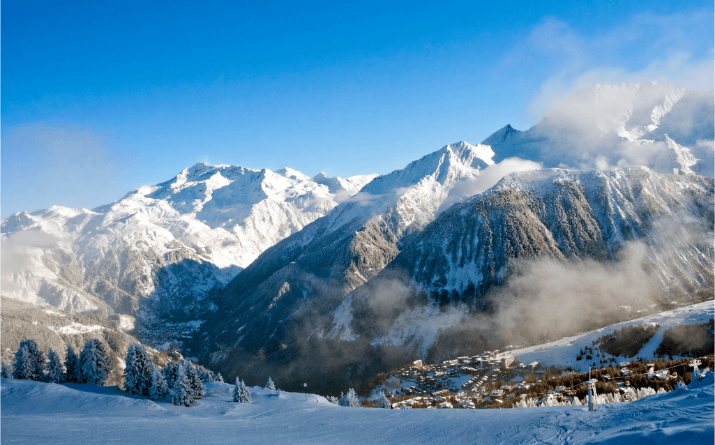 Montanhas nevadas em Courchevel, França, em um dia claro, com uma pequena vila alpina ao sopé das montanhas e florestas de pinheiros cobertas de neve.