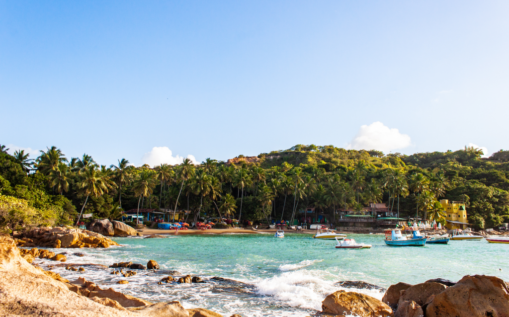 Imagem de uma praia tropical com águas cristalinas, rodeada por palmeiras e barcos coloridos ancorados na costa, capturando a beleza natural da região.