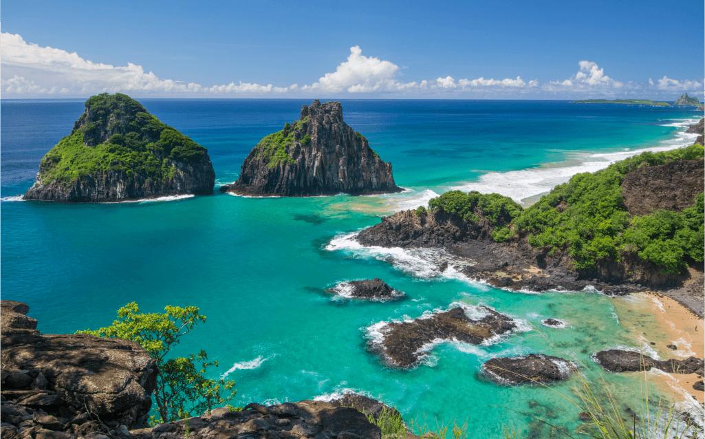 Vista das formações rochosas Dois Irmãos em Fernando de Noronha, com mar azul-turquesa e vegetação ao redor.