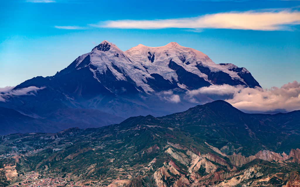 Vista deslumbrante do Monte Illimani na Bolívia, rodeado por nuvens e um céu azul claro, capturando a beleza natural da cordilheira.