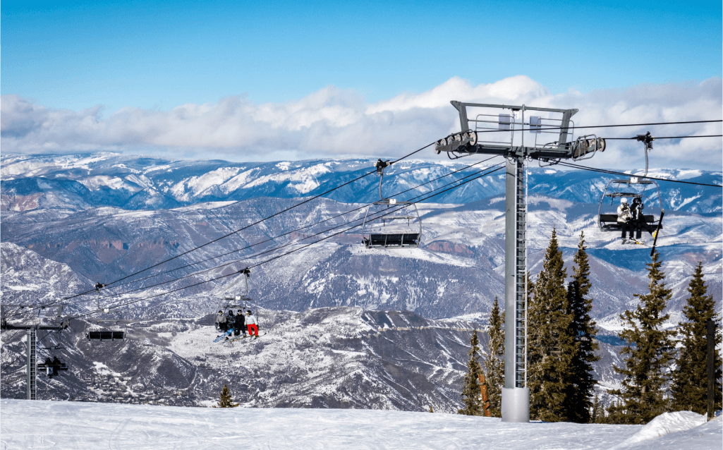 Estação de esqui em Aspen, Colorado, com teleféricos subindo pelas montanhas cobertas de neve, cercadas por um céu azul claro e um cenário de inverno clássico.