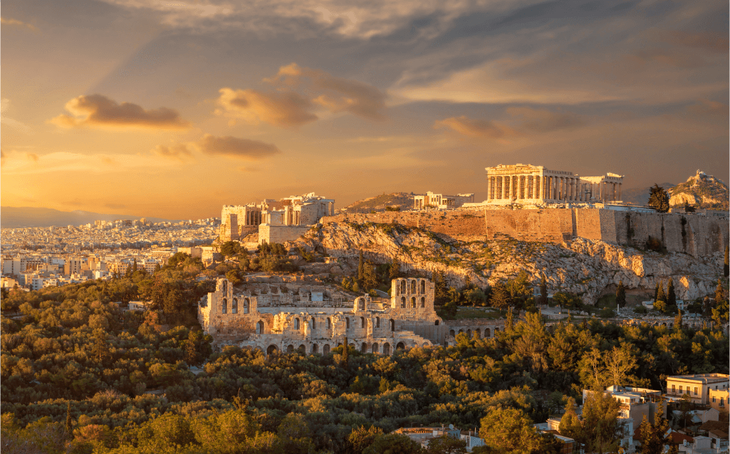 Vista do Parthenon no topo da Acrópole em Atenas, com o pôr do sol iluminando a cidade histórica.