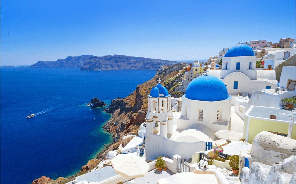 Vista deslumbrante de Santorini, Grécia, com suas casas brancas icônicas e cúpulas azuis no alto de penhascos, com o mar Egeu ao fundo em um dia de céu azul.