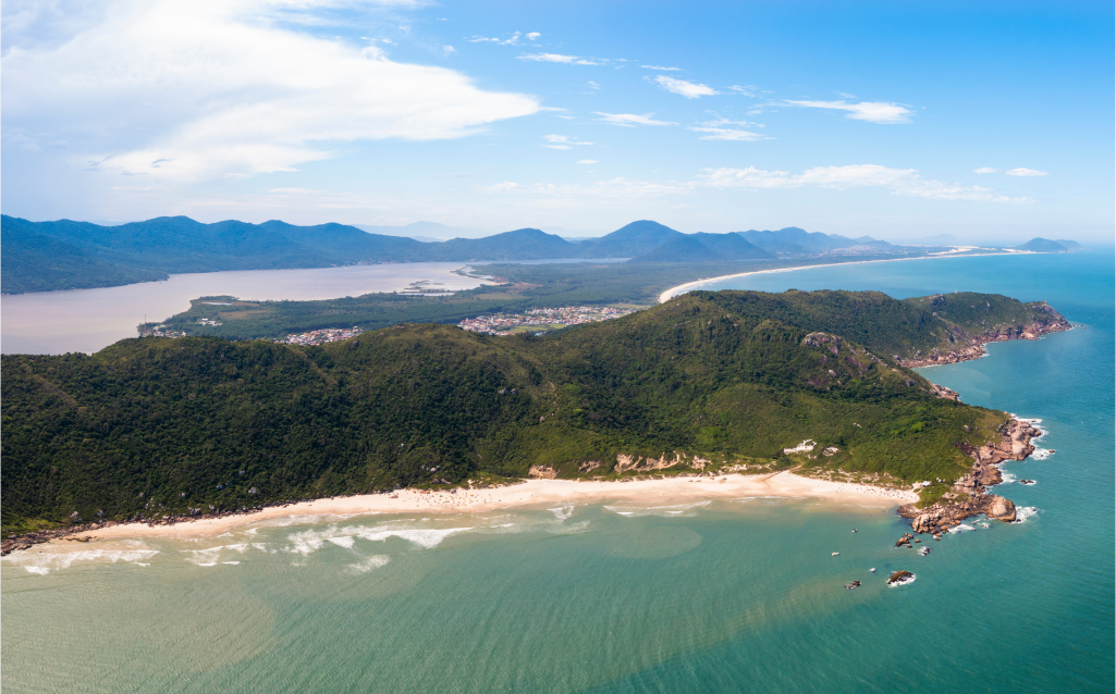 Vista panorâmica de uma praia cercada por vegetação exuberante e montanhas, ideal para relaxar e curtir a natureza.