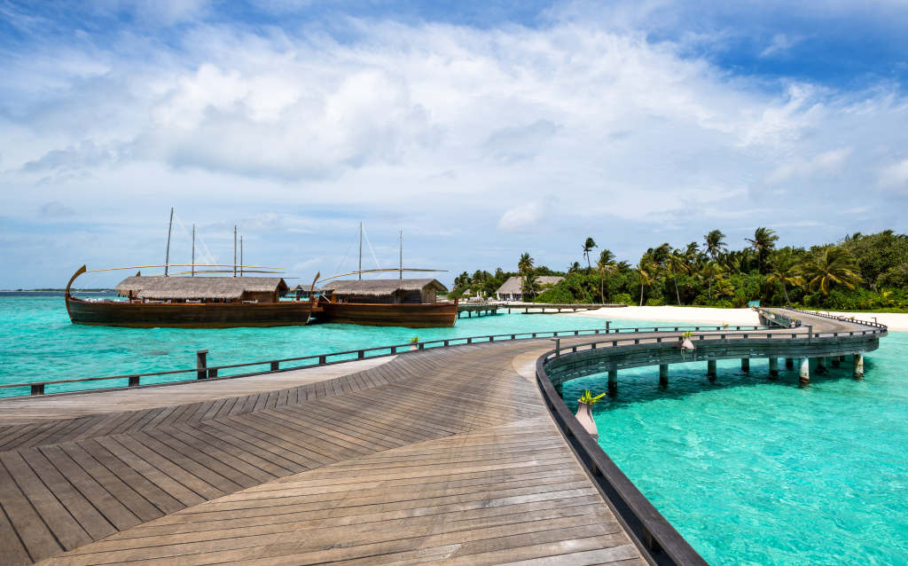 Caminho de madeira em um cenário tropical com águas azuis e barcos ancorados. Ideal para quem busca destinos paradisíacos.