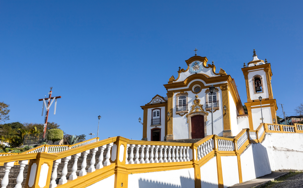 Igreja histórica com detalhes em amarelo e branco, localizada em um dia ensolarado com céu azul, destacando sua arquitetura colonial.