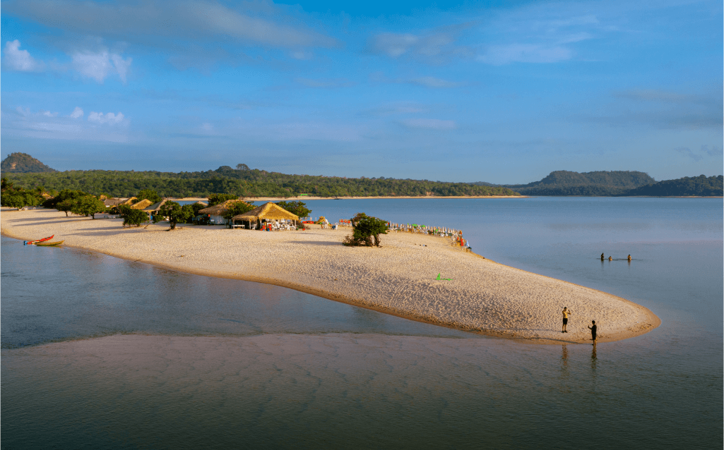 Vista de Alter do Chão, no Pará, com cabanas à beira de uma praia fluvial e águas tranquilas.