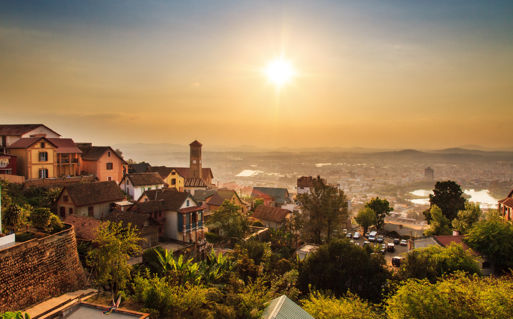 Vista panorâmica da cidade de Antanarivo ao entardecer, com casas coloridas e o sol pôr do sol iluminando a cena. Ideal para quem busca explorar Madagascar.