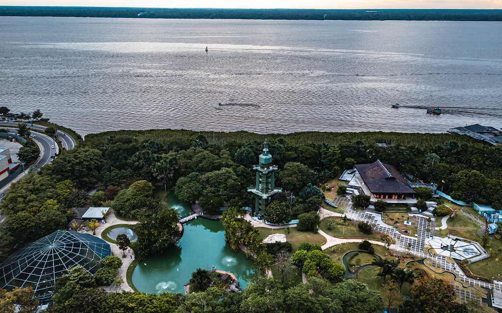   Vista aérea de um parque próximo a um lago, rodeado por árvores e áreas verdes, mostrando um ambiente natural e tranquilo, ideal para relaxamento e lazer.