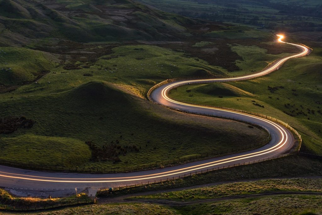 Foto aérea de uma estrada contornando colinas com efeito de time lapse para marcar os faróis de um carro em deslocamento