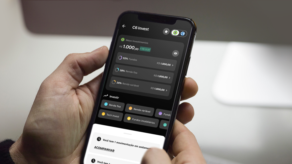 Foto de uma mão segurando um celular onde se pode ver o aplicativo do C6 Bank aberto na aba de investimentos