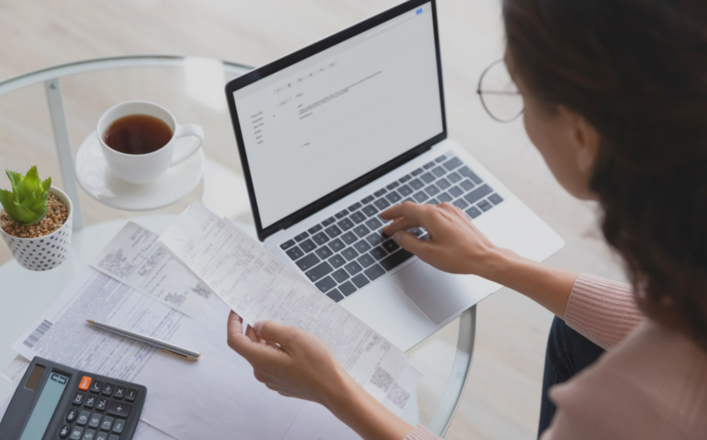 Mulher segurando um papel e olhando o computador com dicas de como fazer balanço financeiro da empresa