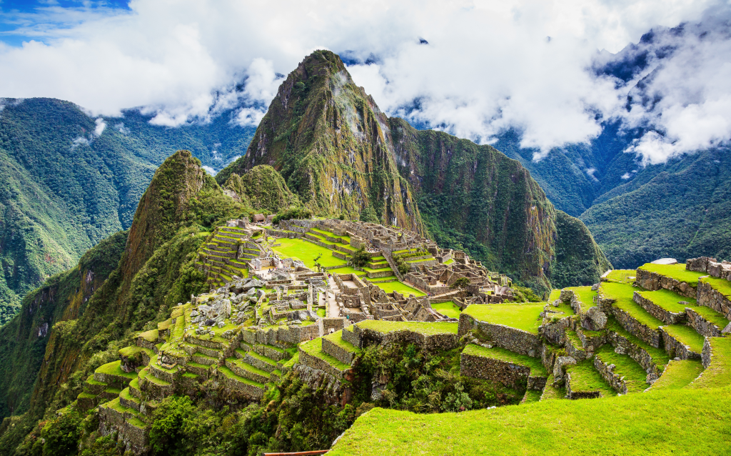 Vista panorâmica de Machu Picchu, com suas ruínas históricas cercadas por montanhas verdes e nuvens, um destino turístico icônico no Peru.