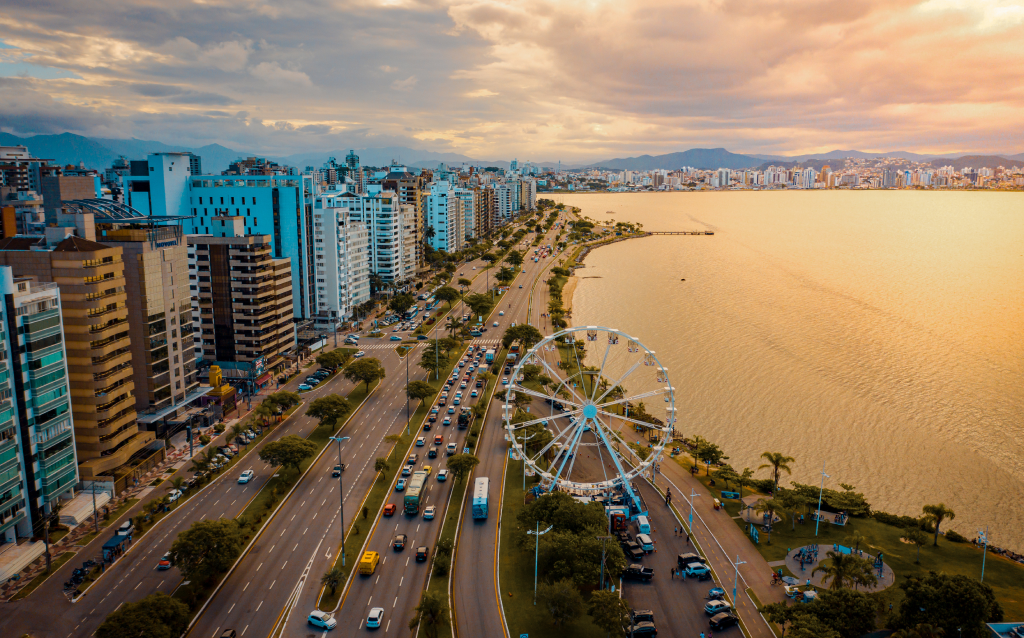 Vista aérea da praia com uma roda-gigante em primeiro plano, mostrando a costa urbana e o entardecer na cidade. Uma bela imagem que destaca a paisagem urbana e natural.