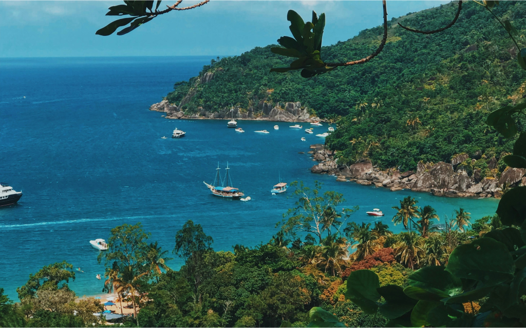 Uma vista deslumbrante de uma baía tropical, com águas cristalinas, barcos ancorando e uma vegetação exuberante ao redor, ideal para férias.