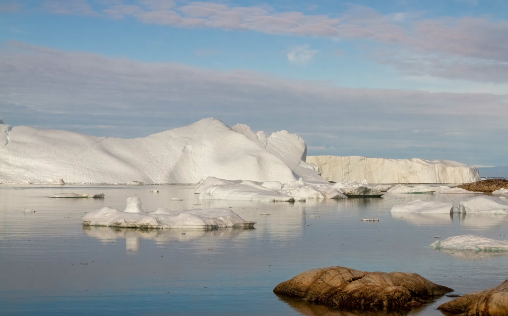 Cenário deslumbrante com icebergs refletindo na água tranquila sob um céu claro, capturando a beleza da natureza e o gelo do Ártico.