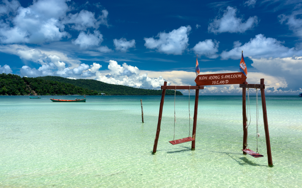   Praia de Koh Rong Samloem, com balanços de madeira sobre águas cristalinas e céu azul, ideal para relaxar e aproveitar a natureza.