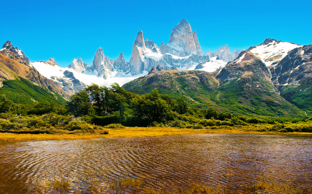 Vista deslumbrante da Cordilheira do Cerro Torre, com picos cobertos de neve refletindo no lago sereno, ideal para amantes da natureza.