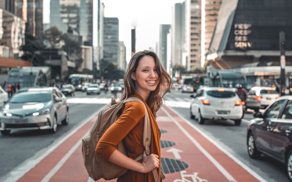 Mochileira segurando sua mala de viagem nas costas parada no meio da Avenida Paulista