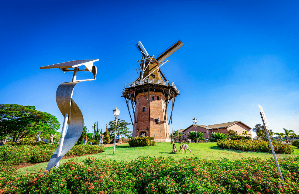 Moinho de vento com fundo de céu azul e monte verde com flores