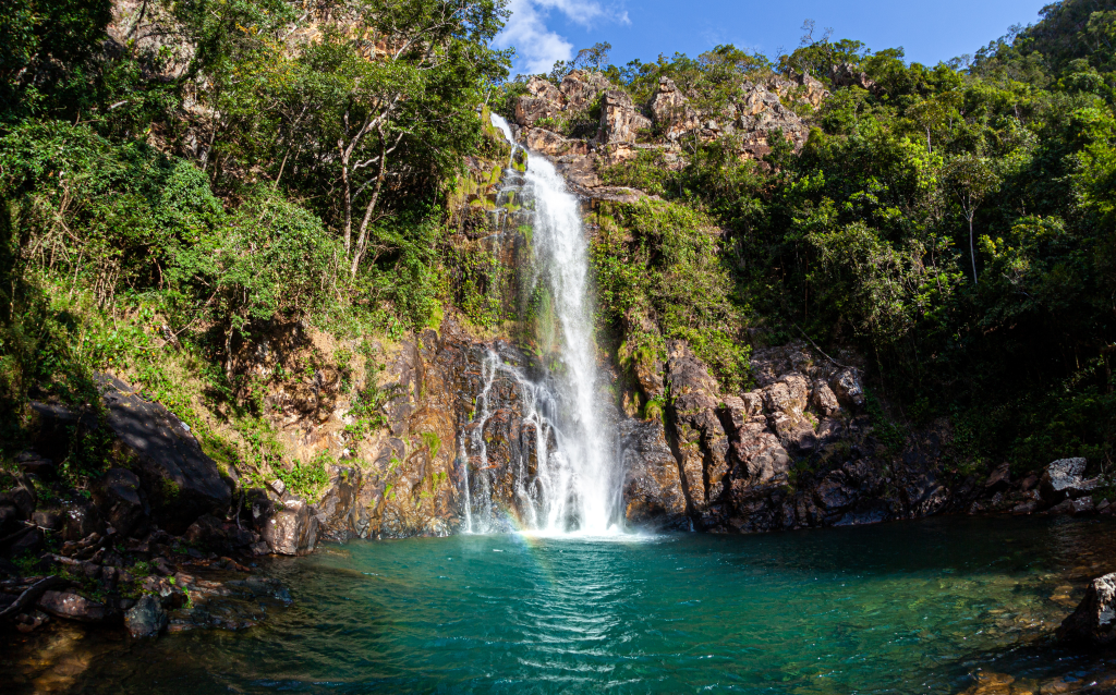 Cascata deslumbrante com água cristalina em meio à natureza exuberante, rodeada por exuberantes árvores verdes e rochas.