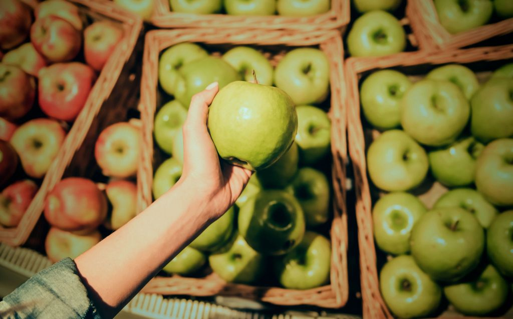 o que é poder de compra | mão segurando uma maçã verde em frente a vários cestos de maçã