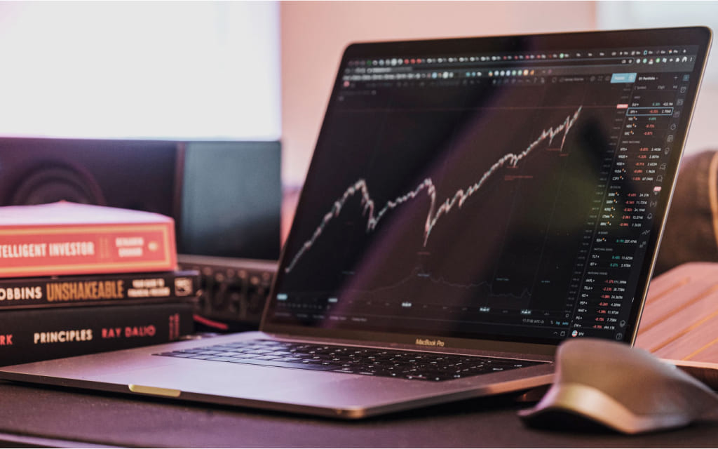 laptop aberto sobre mesa ao lado de livros. a tela mostra um gráfico de linha oscilando, representando o que são fundos multimercado