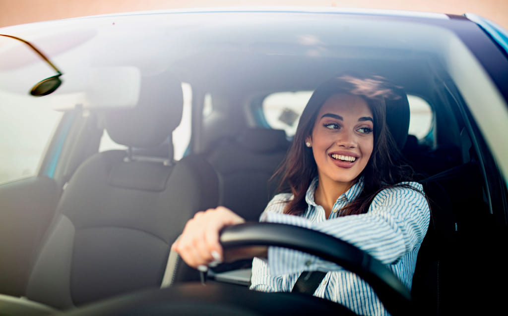 mulher branca sorrindo enquanto dirige carro e pensa em pagar ipva 2023