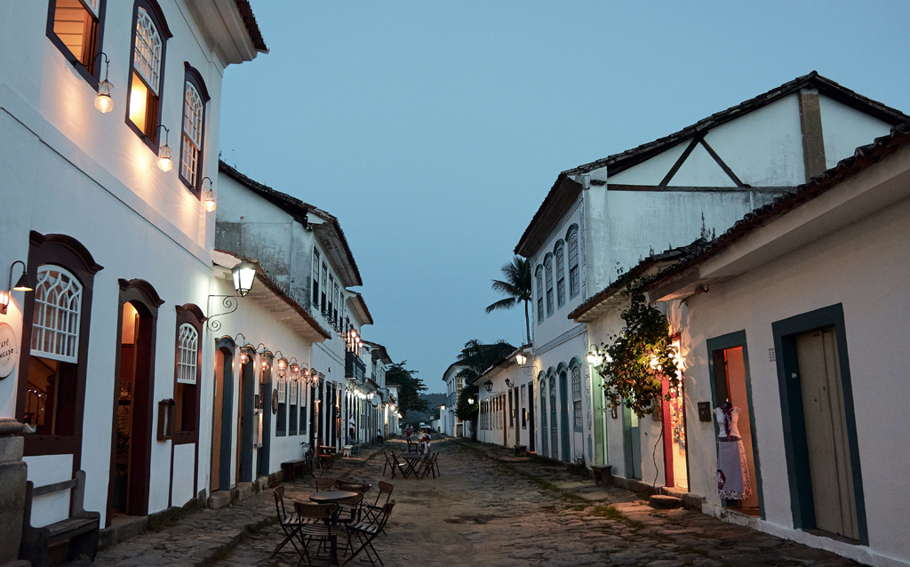 Rua charmosa de um centro histórico, com casas em estilo colonial, luzes aconchegantes e ambiente tranquilo ao entardecer.