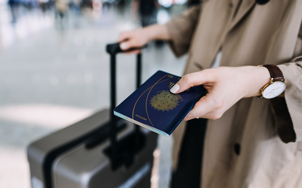 Uma pessoa segurando um passaporte ao lado de uma mala de viagem em um aeroporto, pronta para embarcar em uma nova aventura.