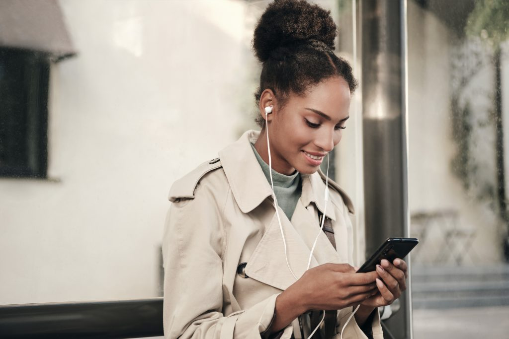 Mulher negra mexendo no celular e fazendo uso de fones de ouvido, pesquisando sobre limite de transferência