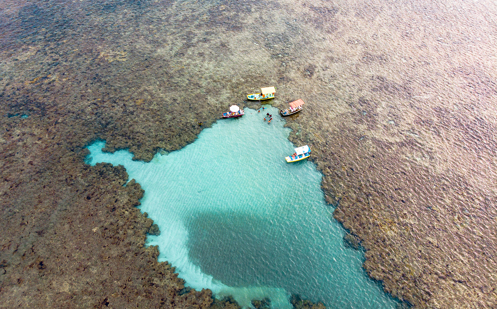 Vista aérea de pequenas embarcações em águas claras sobre um recife de coral, ideal para atividades de mergulho e turismo sustentável.