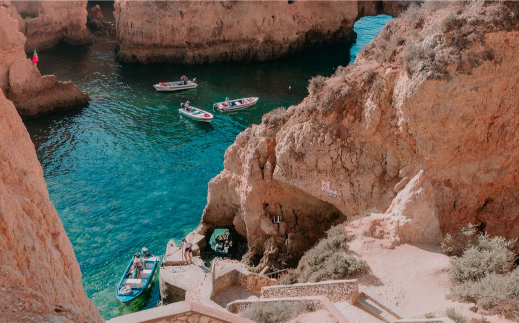 praia em portugal | barcos em meios a pedras antigas e pessoas aproveitando o mar