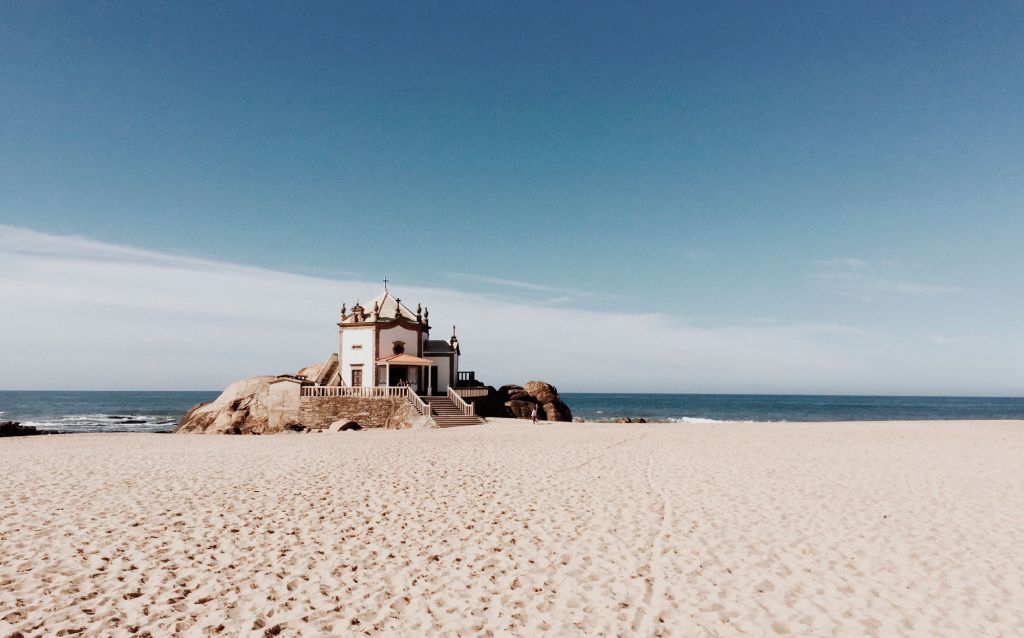 praia em portugal | praia, areia e uma estrutura antiga em meio as pedras