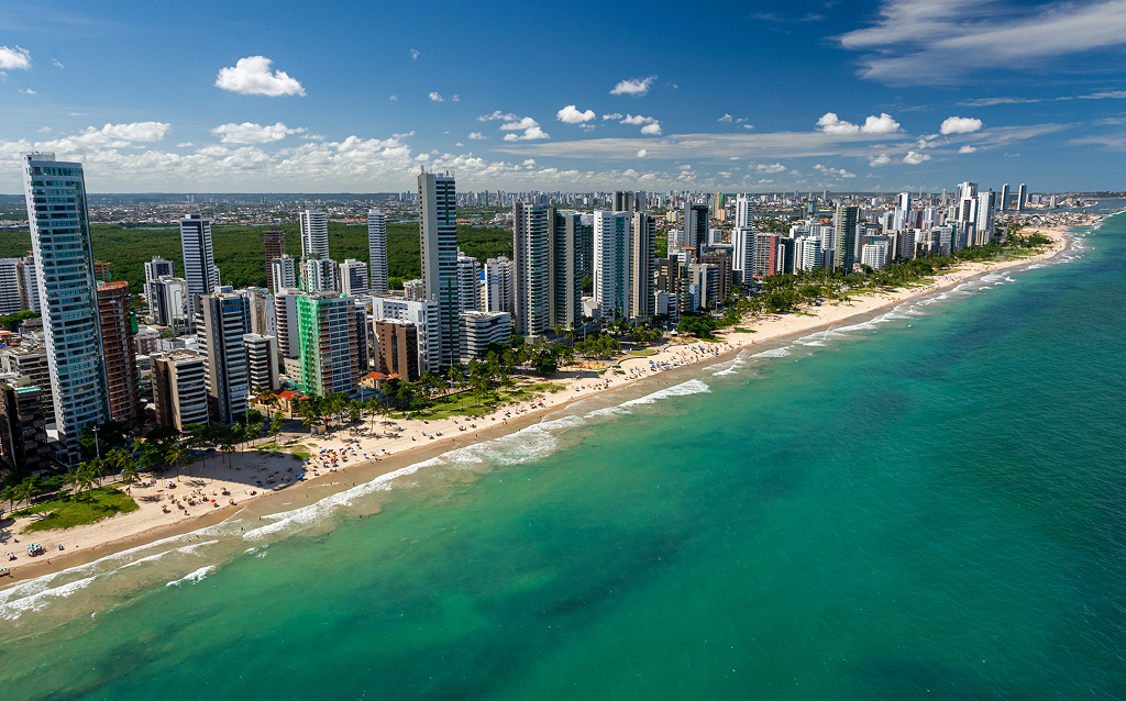 Vista panorâmica da praia com arranha-céus ao fundo, com céu azul e nuvens, ideal para turismo e lazer em áreas urbanas.