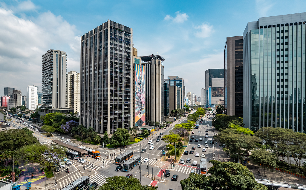   Vista panorâmica da Avenida Paulista em São Paulo, repleta de edifícios modernos, veículos e vegetação ao redor, ideal para quem aprecia o urbanismo brasileiro.