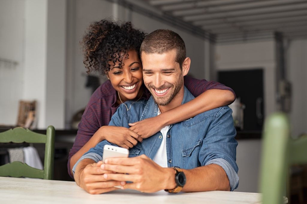 Casal se abraçando, sorrindo e olhando para o celular