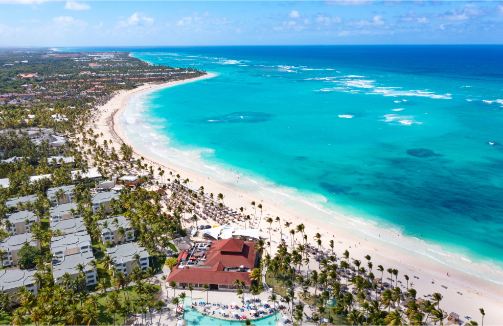 Vista aérea da praia paradisíaca com mar azul e areia fina. Os coqueiros e resorts complementam a paisagem tropical.