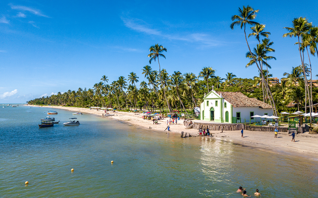 Vista panorâmica de uma linda praia com ondas quebrando, cercada por uma cidade e uma ponte moderna ao fundo, ideal para turismo e relaxamento.